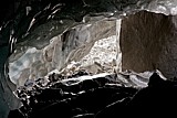 1.8.2010 Morteratschgletscher - Steinquader als Marchstein.<br />- Dies ist die Sicht auf den höher gelegenen Höhleneingang. Die Mächtigkeit dieser Eishöhle wird durch den weit auslaufenden Deckenbogen betont. Alles trieft. Auffällig setzt sich der mannshohe Steinquader in Szene. Bald wird er gänzlich freigelegt sein. Die nahgelegenen Steinbrocken des Bodens stehen in hohem Kontrast zu dem gleißenden Schuttkegel des Moränen-Fußes im Hintergrund und verlieren sich dadurch fast im Schwarz.
